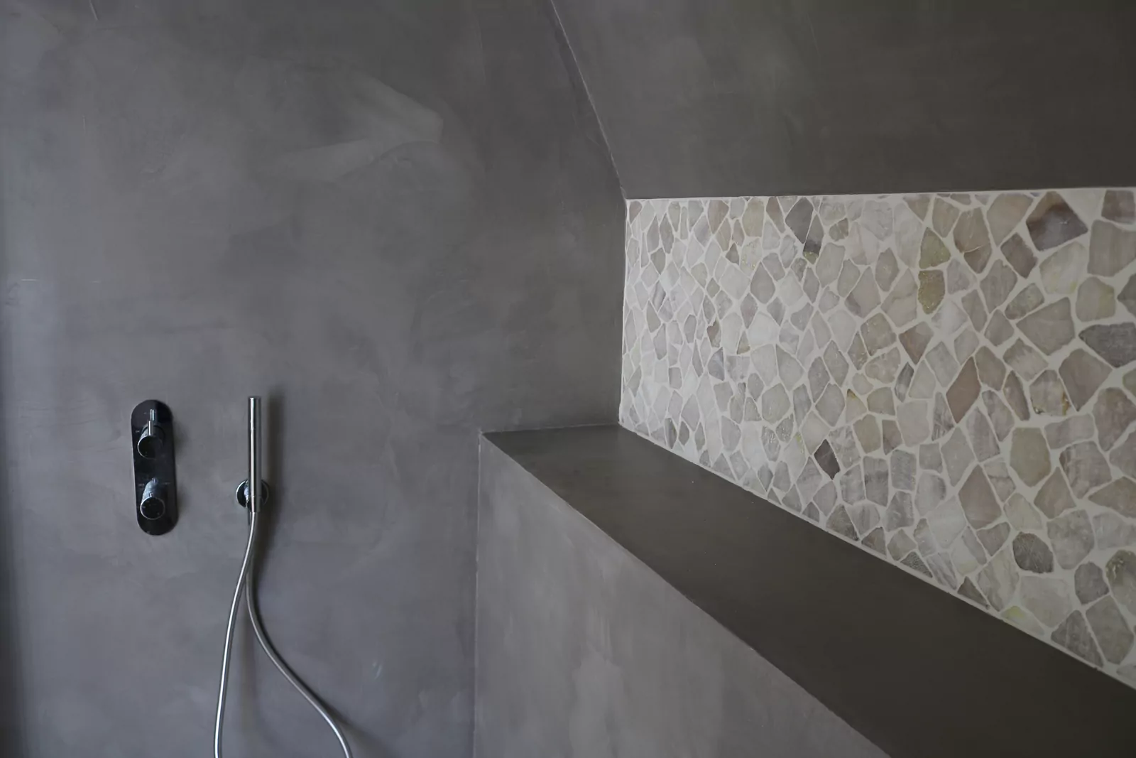Mur de douche en béton ciré gris, sans joint, à côté d'un pan habillé de galets plats